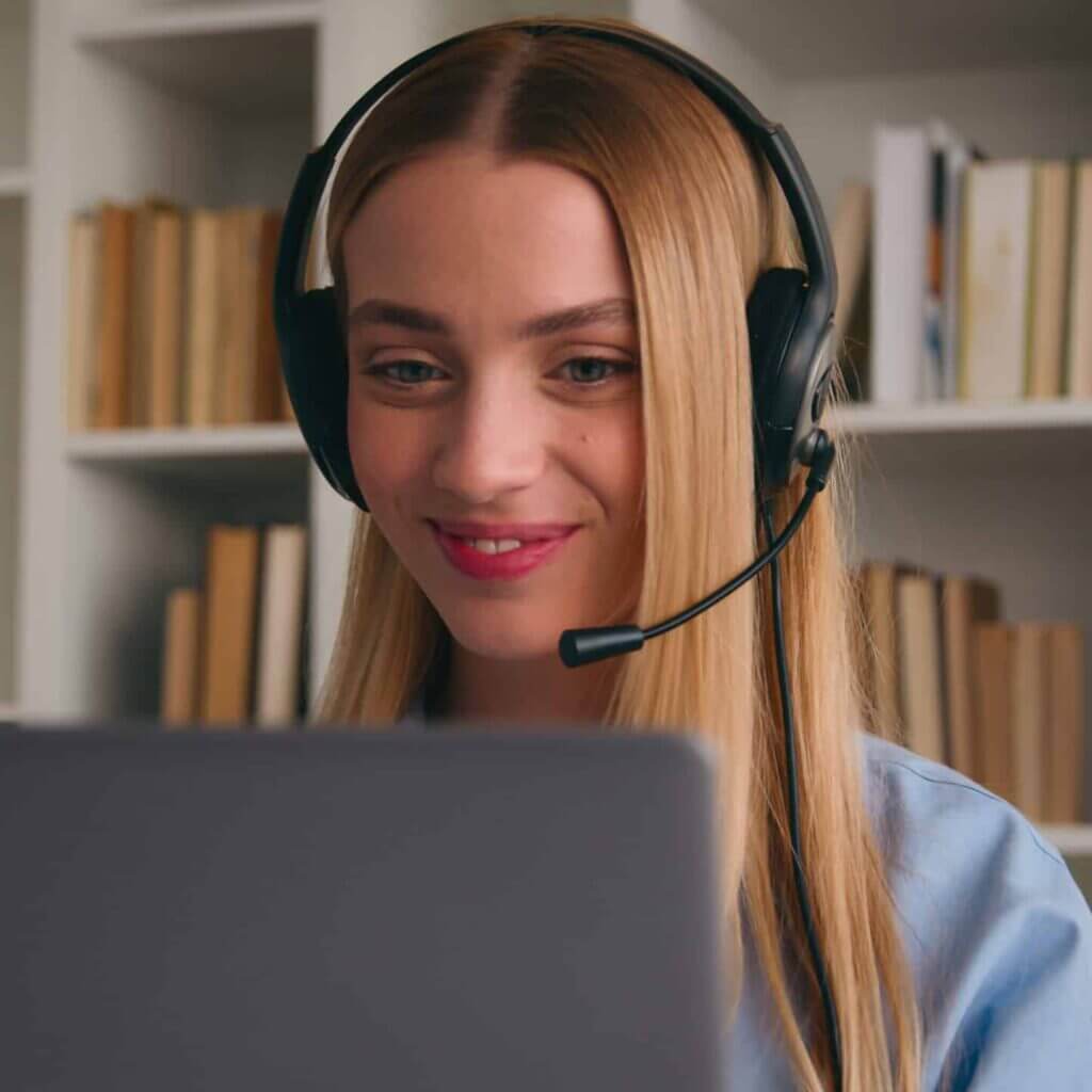 Blonde Mitarbeiterin hat ein Headset auf und spricht mit einem Kunden vor dem Computer